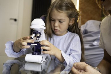 Küçük kız mikroskobu ayarlıyor, örnek topluyor.