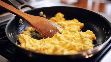 Çırpılmış yumurta, ahşap bir spatulayla siyah bir tavada pişiyor.