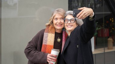 İki kıdemli arkadaş şehir yaşamından zevk alıyor, akıllı telefonla selfie çekiyorlar.