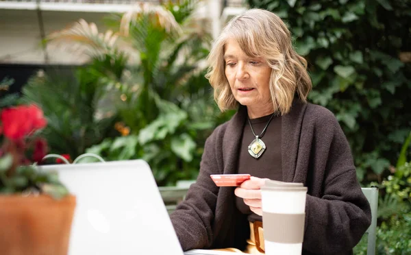 Üst düzey bir kadın açık bir kafeden bilgisayar ve kredi kartı kullanarak online alışveriş yapıyor.