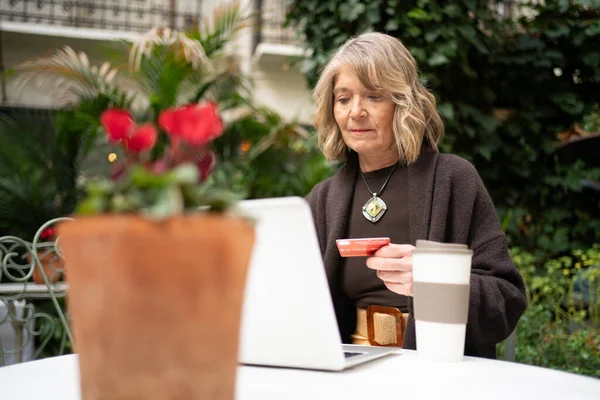 Bahçe masasındaki üst düzey kadın kredi kartını e-ticaret için kullanıyor.