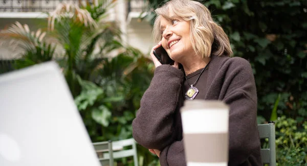 Üst düzey bir kadın açık bir kafede telefonla eğleniyor.