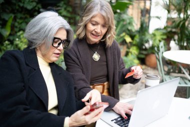 İki yetişkin arkadaş e-ticaret alışverişi için bir dizüstü bilgisayarda işbirliği yapıyorlar.