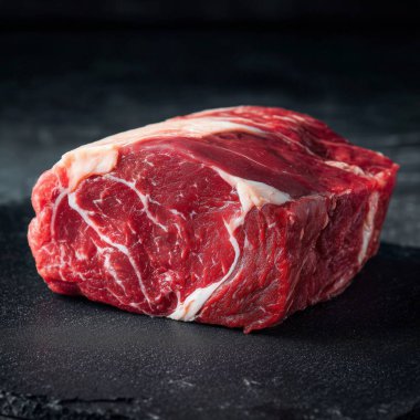 Koyu bir levha yüzeyinde dinlenen çiğ biftek, mermerleri gösteriyor.