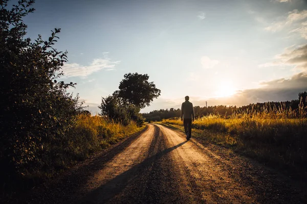 Mężczyzna spacerujący wiejską drogą w stronę zachodzącego słońca — Zdjęcie stockowe