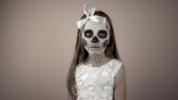 Маленькая девочка в платье с раскрашенным лицом поднимает руку окровавленной головой куклы. — стоковое видео