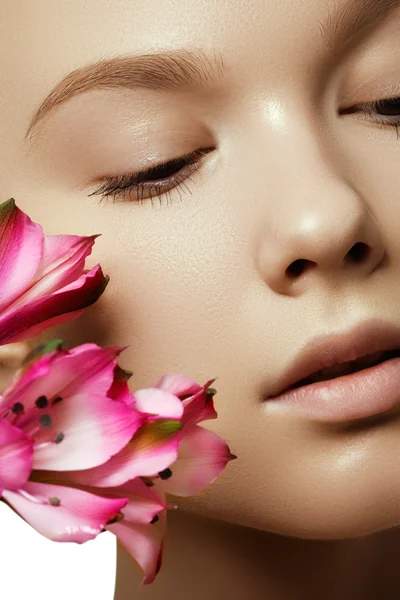 Hermosa mujer joven con una piel brillante perfecta y limpia, maquillaje de moda natural. Mujer de cerca, aspecto de spa fresco. Modelo de cara con flor rosa fresca — Foto de Stock