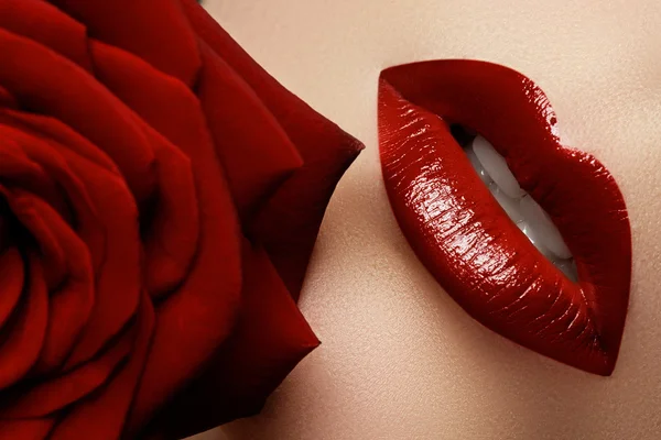 Närbild vackra kvinnliga läppar med ljusa röda makeup. Perfekt ren hud, sexig lip make-up. Vackra spa stående med anbud röd ros blomma. Spa och kosmetika — Stockfoto