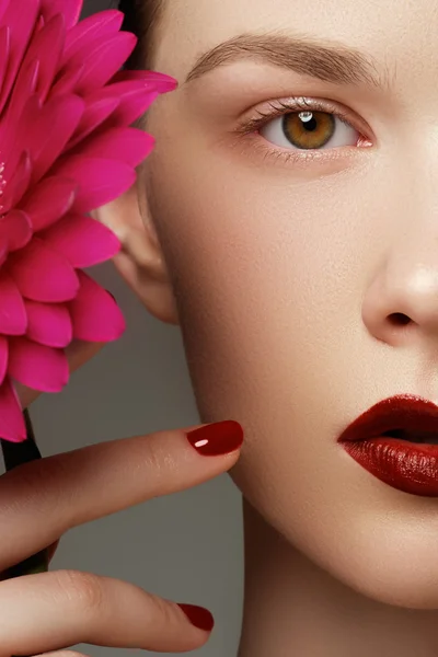 Close-up shot of sexy woman lips with red lipstick and beautiful pink flower. Perfect clean skin, fashion lip make-up. Beautiful spa portrait with tender pink  flower. Spa and cosmetics — Stock Photo, Image