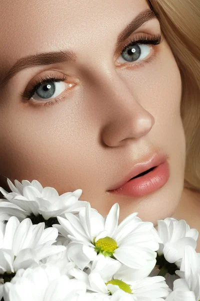 Bella ragazza con fiori in mano su uno sfondo chiaro. Volto di bellezza della giovane bella donna con fiore. Ragazza su sfondo bianco — Foto Stock