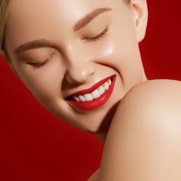 Belleza retrato de mujer joven sobre fondo rojo. Hermosa chica modelo con maquillaje de belleza, labios rojos, piel fresca perfecta. Atractiva dama rubia con ojos marrones. Concepto de cuidado de la piel y la juventud — Foto de Stock