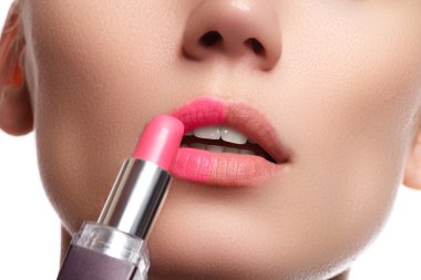 Close up portrait of attractive lips of beautiful woman. Rouging her lips with pink mate lipstick. The lady is gently smiling. Close-up of woman applying pink lipstick on her lips