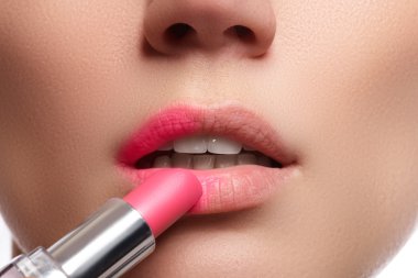 Close up portrait of attractive lips of beautiful woman. Rouging her lips with pink mate lipstick. The lady is gently smiling. Close-up of woman applying pink lipstick on her lips