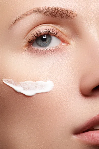 Hermosa mujer joven con la piel limpia y fresca de cerca. Hermosa cara de mujer cerca del estudio en blanco. Mujer joven con crema cosmética en una cara limpia y fresca. Concepto de cuidado de la piel — Foto de Stock