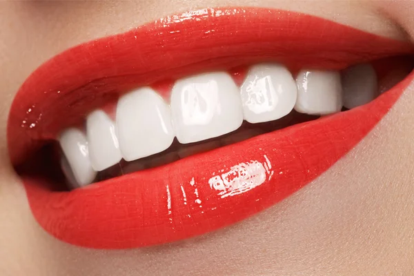 Close-up happy female smile with healthy white teeth, bright red lips make-up. Cosmetology, dentistry and beauty care. Macro of woman's smiling mouth