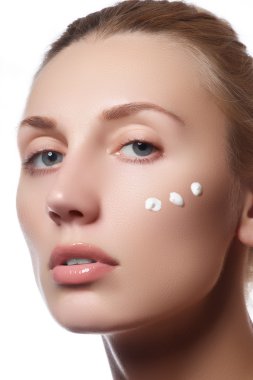 Güzel yüzünü bir yanağına kozmetik krem ile genç kadın. Cilt bakım kavramı. Portre portre üzerinde beyaz izole. Yakın çekim Genç güzel yüzünü uygulayarak kızın nemlendirici krem.