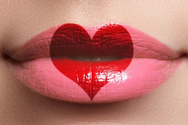 Un beso de corazón en los labios. Belleza sexy labios llenos con pintura en forma de corazón. Día de San Valentín. Hermoso maquillaje. Lápiz labial y brillo de labios — Foto de Stock