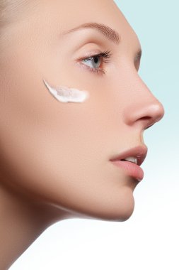 Güzel yüzünü bir yanağına kozmetik krem ile genç kadın. Cilt bakım kavramı. Portre portre üzerinde beyaz izole. Yakın çekim Genç güzel yüzünü uygulayarak kızın nemlendirici krem.