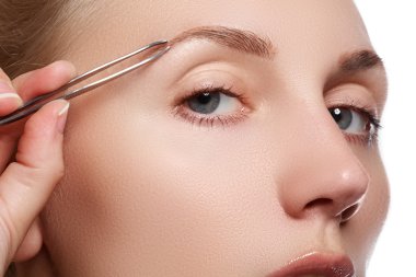 Make-up & cosmetics. Closeup portrait of beautiful woman model face with clean skin. Closeup of face, woman plucking eyebrows depilating with tweezers. Beautiful woman tweezing eyebrows.