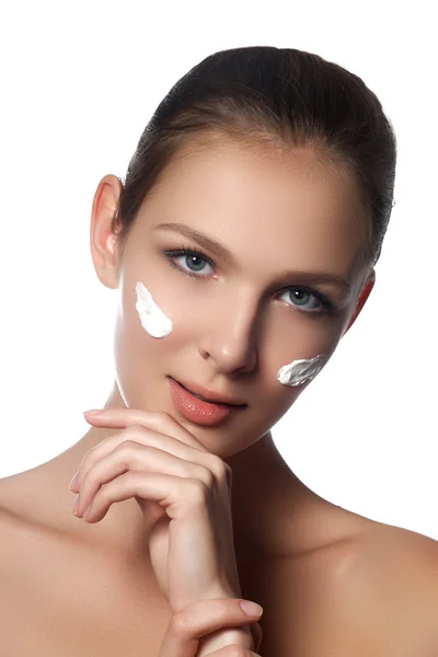 Cura della pelle signora mettendo crema per il viso. Attraente ragazza bruna su sfondo bianco. Bellissimo viso di giovane donna con crema cosmetica su una guancia. Il concetto di cura della pelle. Prodotti per la cura della pelle — Foto Stock