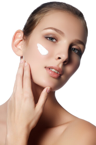 Beautiful face of young woman with cosmetic cream on a cheek. Skin care concept. Closeup portrait isolated on white. Close-up young beautiful face of girl applying moisturize cream