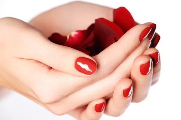 Hermosas uñas de dedo hembra con uña roja de cerca en pétalos. Manicura perfecta. Las manos de la mujer con las uñas rojas manicura primer plano y rosa. Cuidado de la piel y las uñas — Foto de Stock