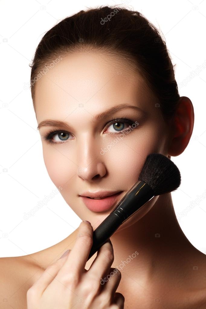 Beauty model with makeup brush. Bright make-up for brunette woman with blue eyes. Beautiful face. Perfect Skin. Applying makeup
