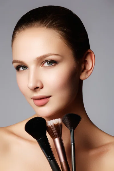 Closeup portrait of a woman applying dry cosmetic tonal foundation on the face using makeup brush. Beautiful woman with makeup brushes near her face - isolated on white — Zdjęcie stockowe