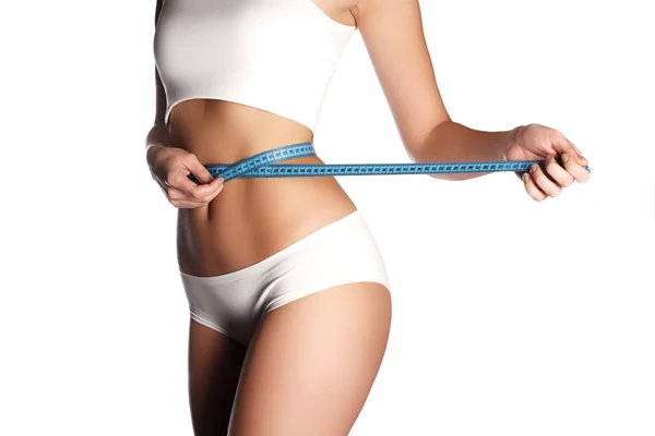 Мера на теле женщины на белом фоне. Модное фото сексуальной молодой женщины в нижнем белье с тонким телом, сидящей на диете и измеряющей талию сантиметровой лентой — стоковое фото