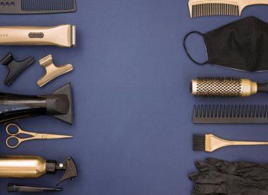 Mavi arka planda siyah ve altın rengi kuaför aletleri. Berber malzemeleri, makas, toka, eldiven, maske, tarak ve saç kurutma makinesi çerçevesi. Metin için ortalanmış boşluk.