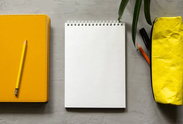 An empty white notebook, a book, and a yellow pencil case. Top view of objects.