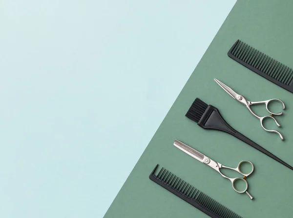 Hairdressing tools on a green background and a blue sheet with space for text. Black and steel hair salon accessories, comb and scissors