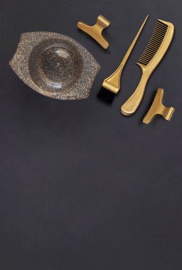 Koyu gri arka planda, fotokopi alanı olan saç boyama için altın kuaför aletleri. Masanın üzerinde kuaför, tarak, fırça, kase ve klipslerin aksesuarları var..