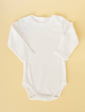 Sarı arka planda beyaz bebek kıyafetleri, düz yatış.. 