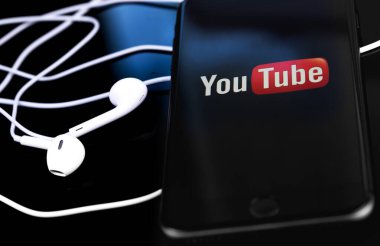 Ekran akıllı telefonunda YouTube logosu ve kulaklıklar yakın plan. YouTube herkesin izleyebileceği ücretsiz bir video paylaşım uygulamasıdır. Moskova, Rusya - 10 Haziran 2020