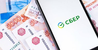 Rus Rublesi banknotlarının arka planındaki akıllı telefon ekranında Sber (Sberbank) logosu. Sberbank, Rusya, Orta ve Doğu Avrupa 'nın en büyük uluslararası, evrensel bankasıdır. Moskova, Rusya 24 Eylül 2020