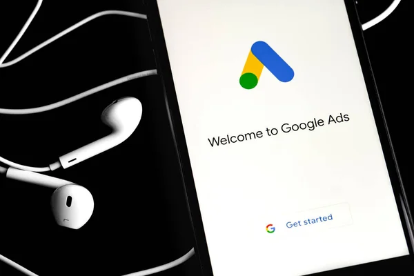 Google Ads (AdWords) logo on the screen smartphoneand and Earpods on black background. Google Ads is a service of contextual, basically, search advertising from Google. Moscow, Russia - June 10, 2020