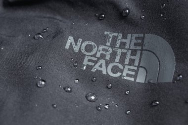 The North Face logo on black jacket with water drops. The North Face is an American outdoor product company specializing in outerwear. Moscow, Russia - July 18, 2020 clipart