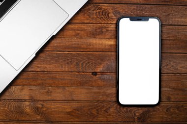 iPhone 12 Pro Max with blank white screen, MacBook notebook on wood desk closeup. Apple is a multinational technology company. Moscow, Russia - December 5, 2020