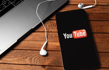 Ekran iPhone 'undaki YouTube mobil logosu MacBook ve Earpod' ların kulaklıkları kapalı. YouTube herkesin izleyebileceği ücretsiz bir video paylaşım uygulamasıdır. Moskova, Rusya 5 Aralık 2020