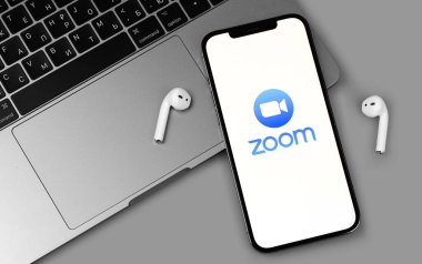 Mobil logo uygulamasını AirPods ve MacBook klavyeli akıllı telefon iPhone ekranına yakınlaştır. Zoom Video Communications, uzaktan konferans hizmeti veren bir şirket. Moskova, Rusya - 12 Haziran 2021