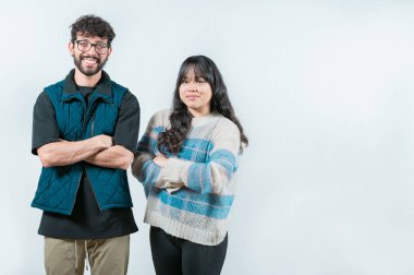 Kollarını kavuşturmuş gülümseyen genç bir çift kameraya bakıyor, izole edilmiş. Kollarını kavuşturup izole edilmiş neşeli, etnik çeşitlilikte genç bir çift.