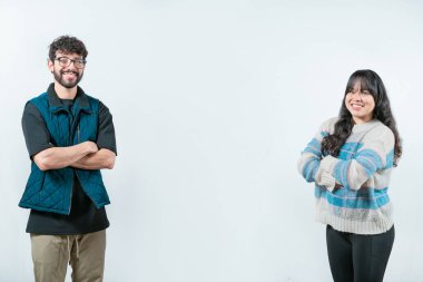 Kollarını kavuşturmuş, izole edilmiş neşeli, etnik çeşitlilikte genç bir çift. Kollarını kavuşturmuş gülümseyen genç bir çift kameraya bakıyor.