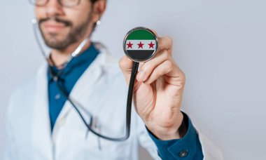 Suriye bayrağıyla steteskop tutan doktor. Suriye sağlık ve bakım konsepti. Steteskopta Suriye bayrağı