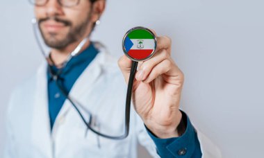 Ekvator Gine bayrağıyla steteskop tutan doktor. Ekvator Ginesi sağlık ve bakım konsepti. Steteskopta Ekvator Gine bayrağı