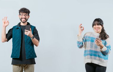 Cep telefonu tutan ve el kol hareketi yapan, izole edilmiş bir çift. Mutlu genç çift ellerinde telefonla el kol geziyor.