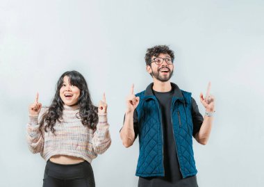 Şaşırmış genç çift izole edilmiş uzayı işaret ediyor. Mutlu genç çift bir reklama işaret ediyor.