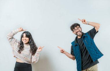 Mutlu Asyalı genç çift izole edilmiş bir ilana işaret ediyor. Neşeli genç çift uzayı işaret ediyor