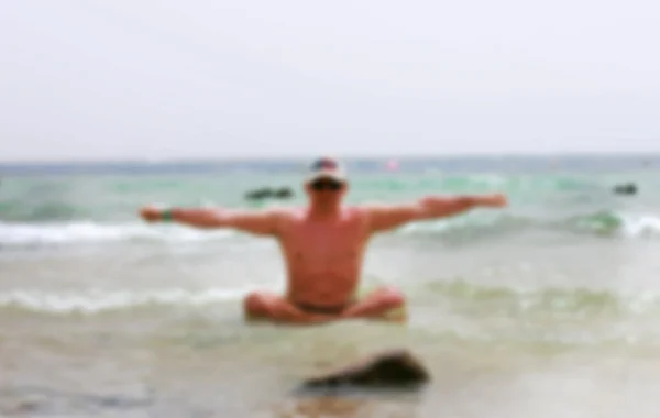 Мужчина на пляже, занимающийся йогой, размыт — стоковое фото
