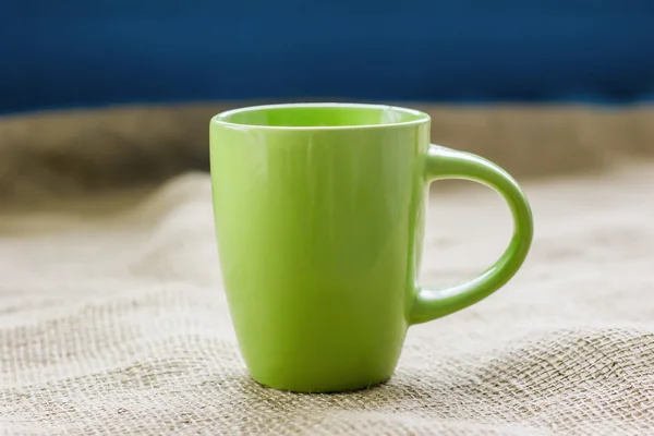 Зеленая чашка на столе у окна на мешковине изолированы, с — стоковое фото